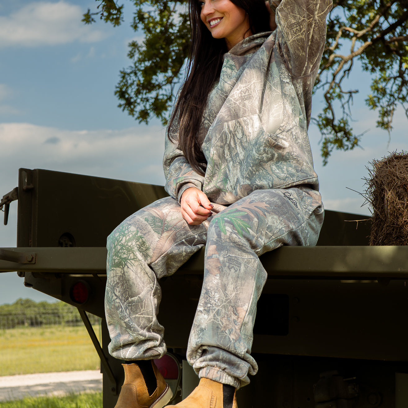 Person wearing camouflage clothing sitting on a vehicle in an outdoor setting
