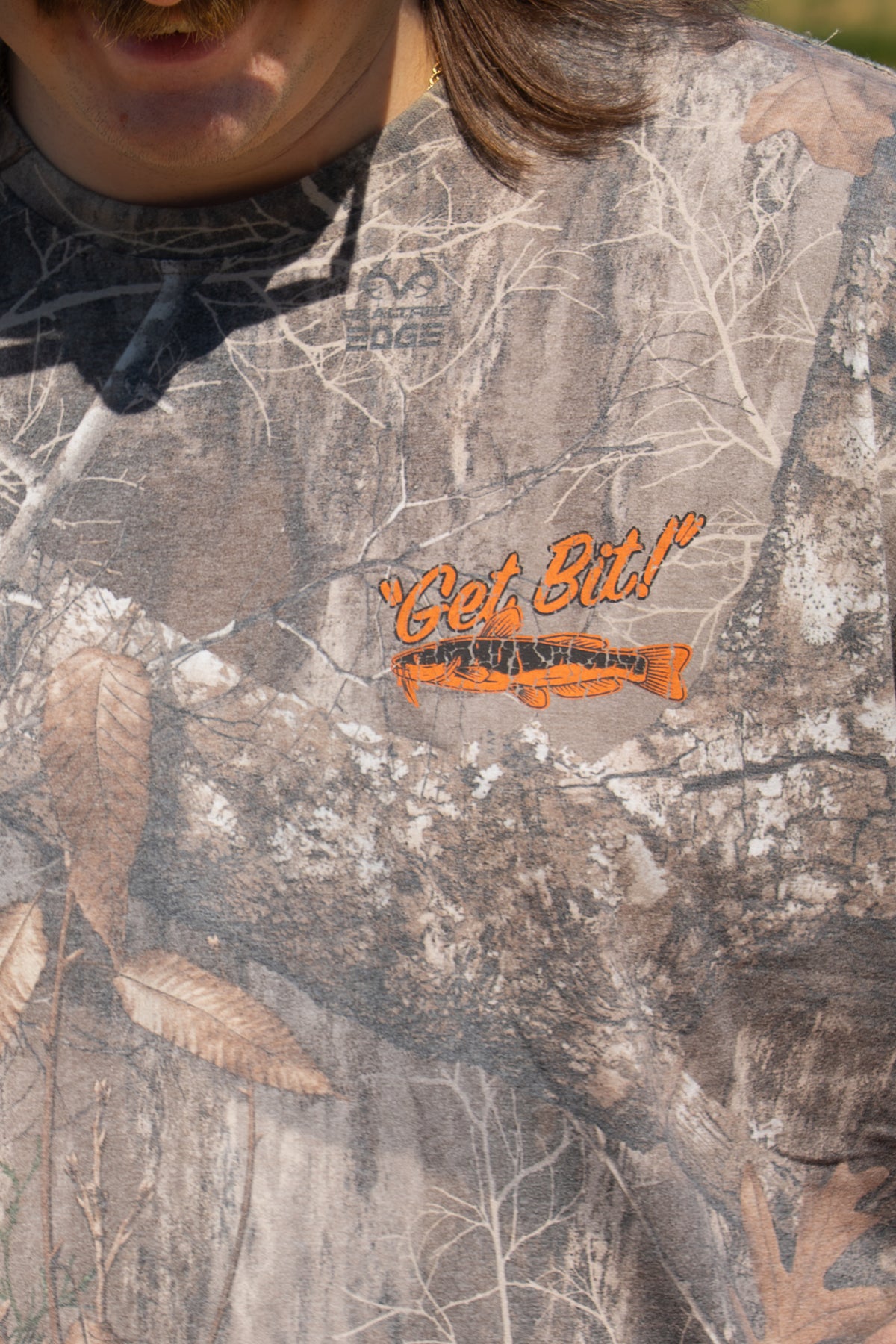 Closeup of left chest of camo tee with fish graphic and "Get Bit!" text