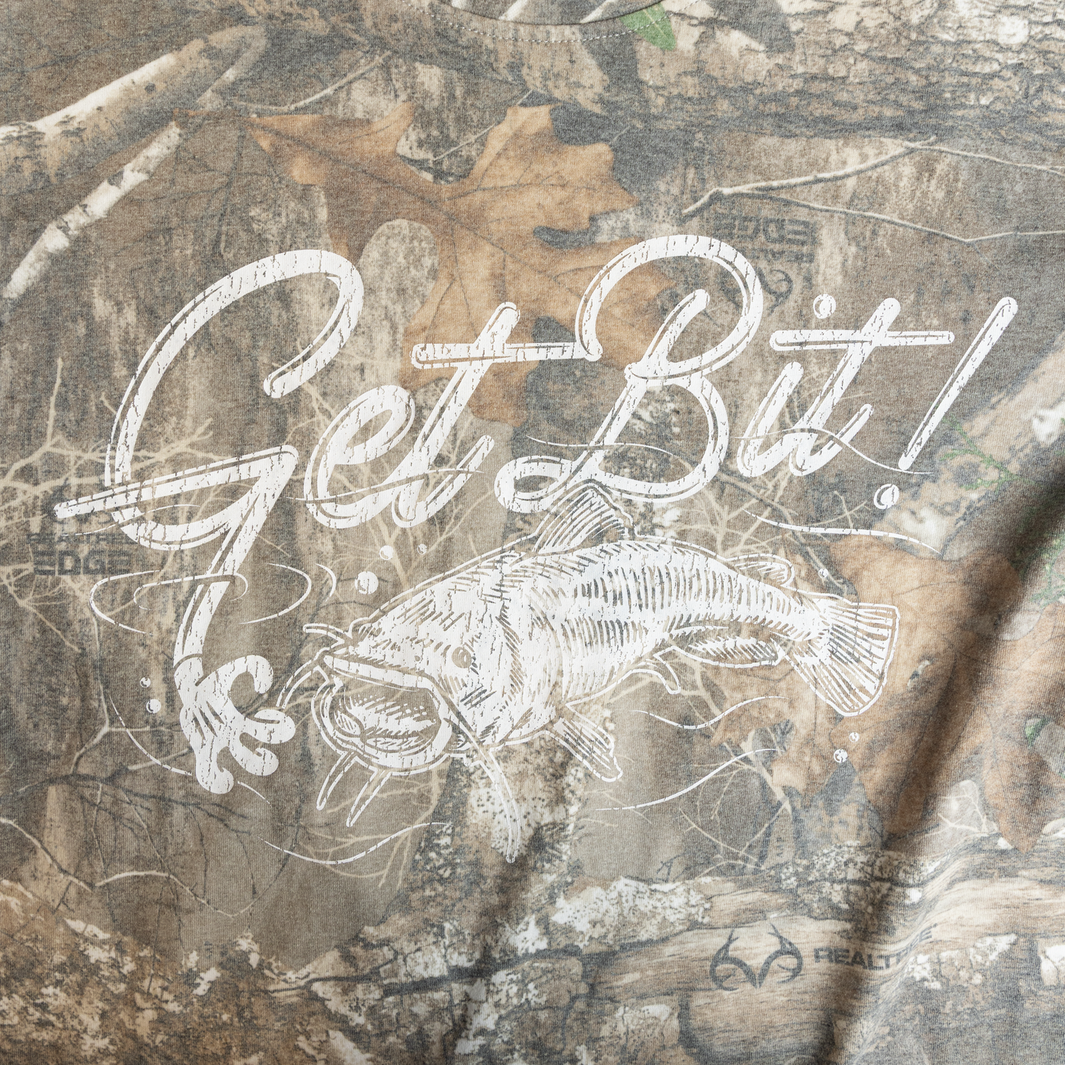 closeup of "Get Bit!" logo with fish on camo tee