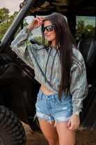 Woman in a camouflage hoodie and denim shorts standing next to a vehicle.
