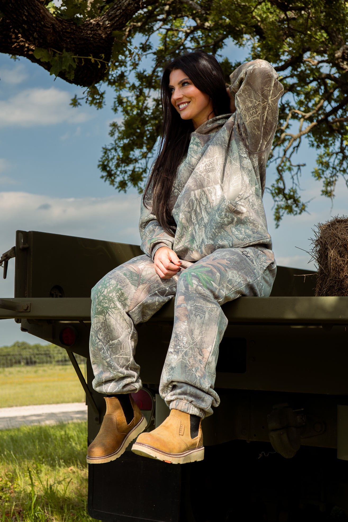 Person wearing camouflage clothing sitting on a vehicle in an outdoor setting