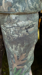 Close-up of camouflage pants with a "Get Bit!" logo on a natural background