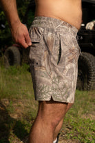 Person wearing camouflage shorts in an outdoor setting with a vehicle in the background.