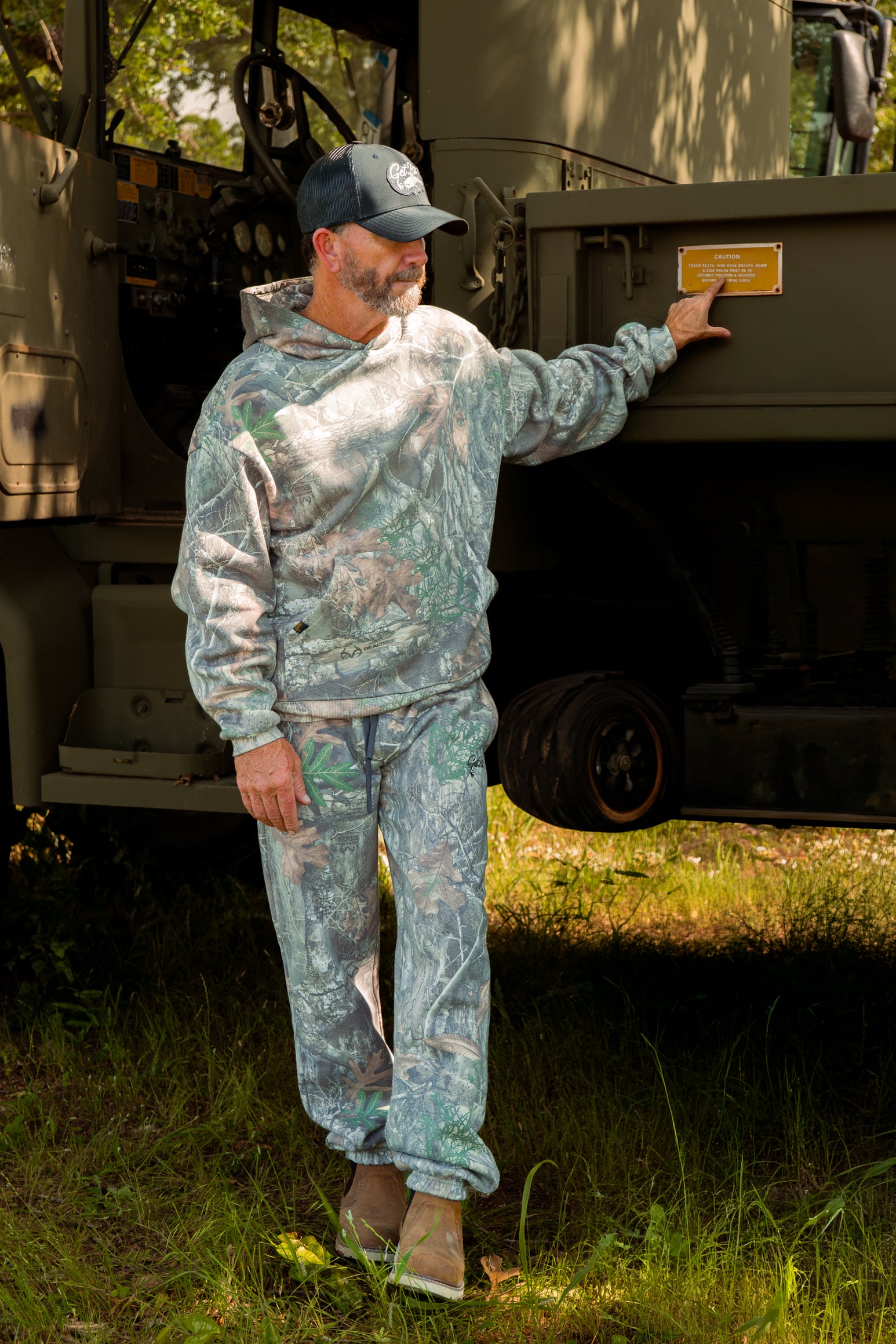 Man in camouflage hoodie and pants outdoors.