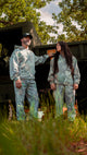 Two people in full camouflage outfits standing outdoors with a vehicle in the background.
